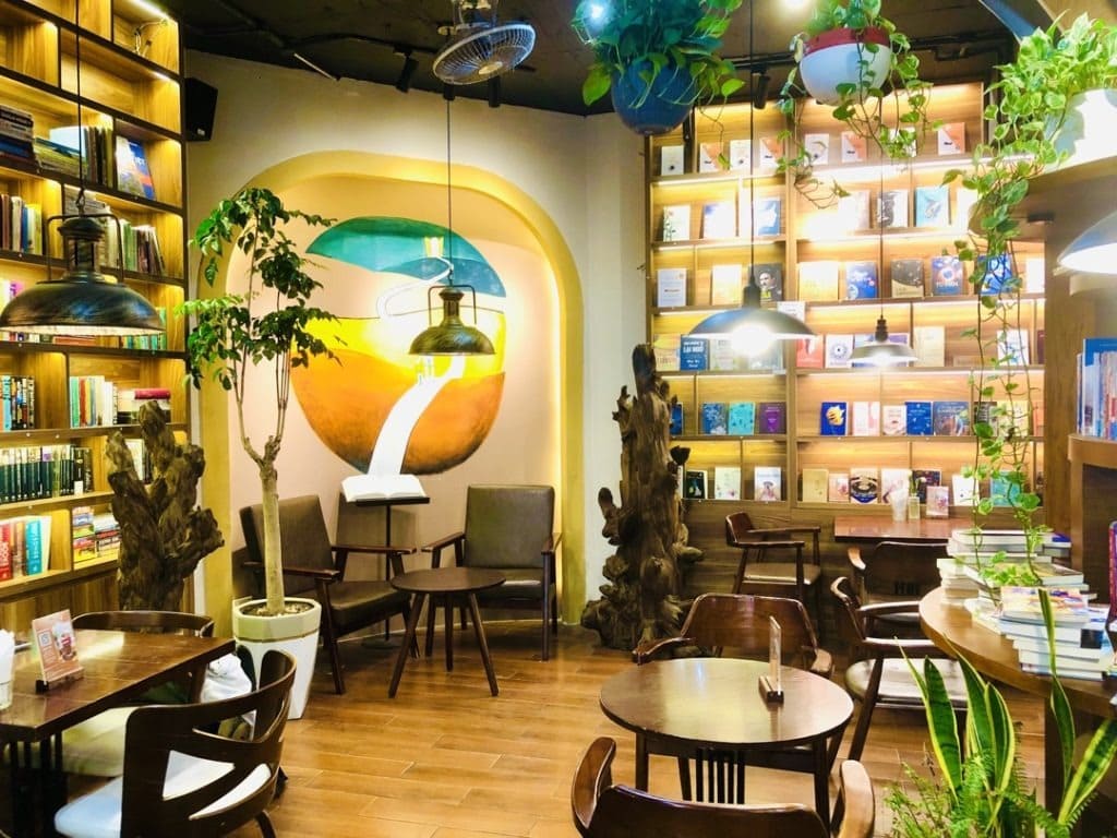 Quán cafe sách phong cách rustic với kệ sách gỗ thô, bàn sắt và cây xanh mộc mạc